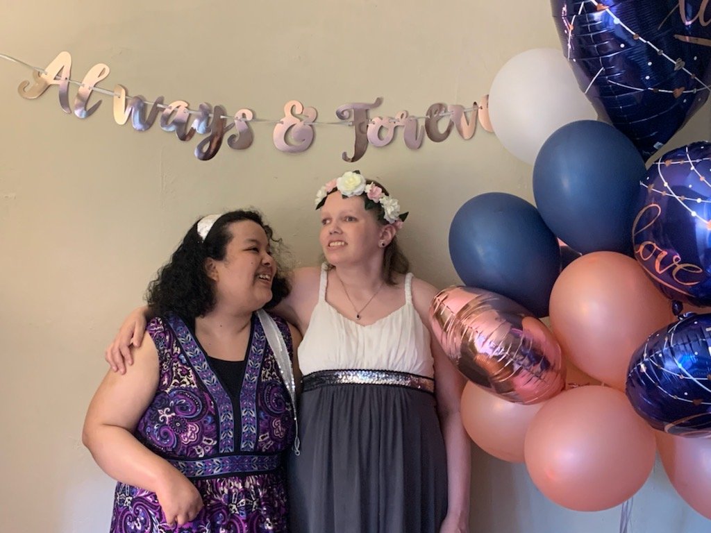 Michelle and I stand smiling under an "Always & Forever" banner, with one wearing a flower crown. Pink, blue, and heart-shaped balloons are on the right side of the image.